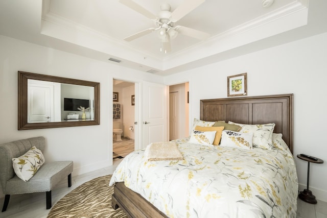 bedroom featuring a raised ceiling, ornamental molding, and ensuite bath