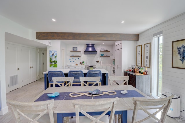 dining room with light wood finished floors, beamed ceiling, visible vents, and wooden walls