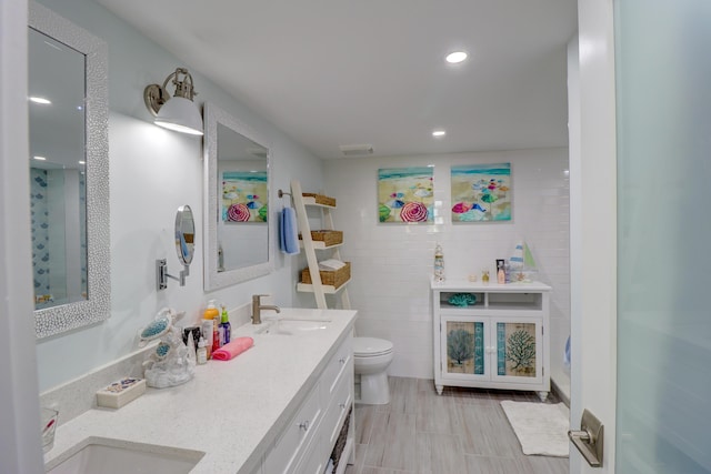 full bath featuring double vanity, toilet, tile walls, and a sink