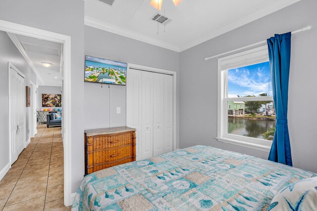 bedroom with light tile patterned floors, ceiling fan, a water view, ornamental molding, and a closet