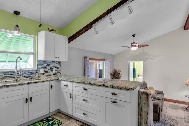 kitchen featuring sink, tasteful backsplash, vaulted ceiling, kitchen peninsula, and white cabinets