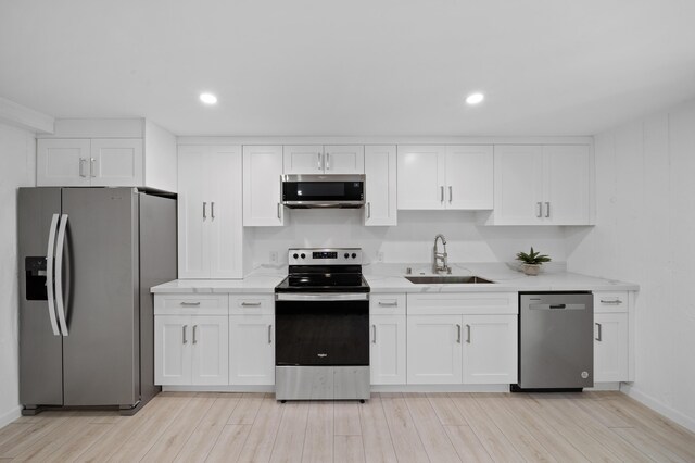 kitchen with appliances with stainless steel finishes, a sink, white cabinets, light wood-style floors, and recessed lighting