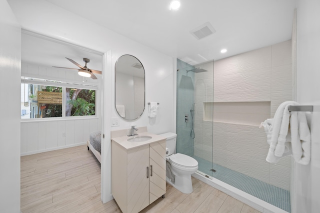 bathroom featuring wood finished floors, a walk in shower, vanity, ceiling fan, and toilet