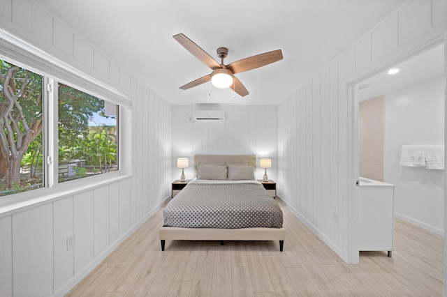 bedroom with a wall unit AC, light wood-style floors, a decorative wall, and ceiling fan