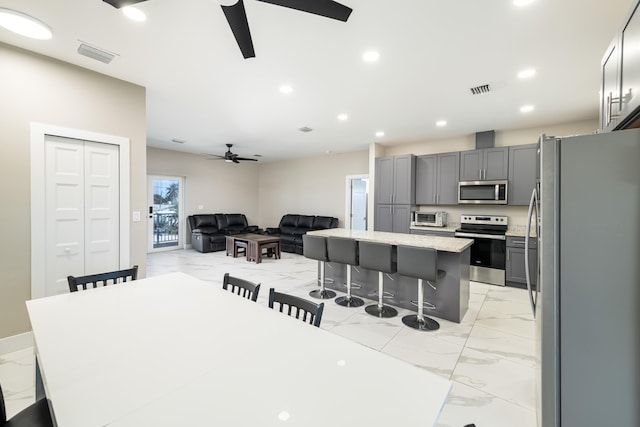 kitchen featuring marble finish floor, a breakfast bar area, a ceiling fan, and stainless steel appliances