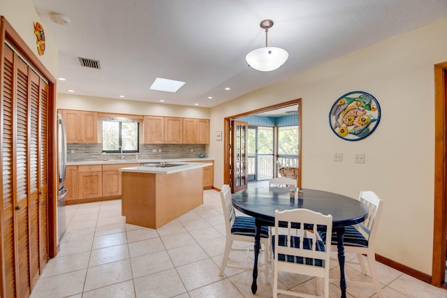 kitchen with pendant lighting, light brown cabinetry, sink, backsplash, and a center island