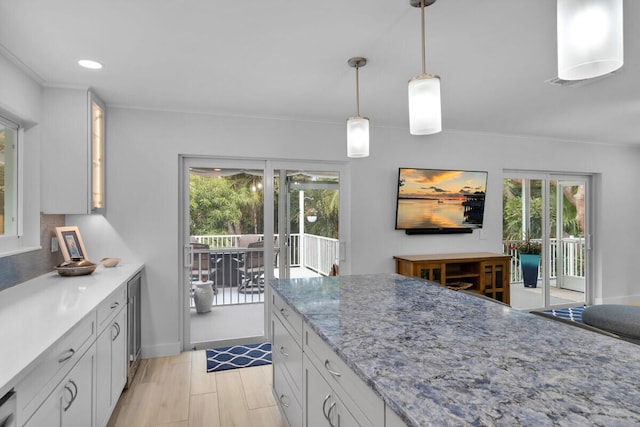 kitchen with hanging light fixtures, white cabinetry, light stone countertops, and light wood-type flooring