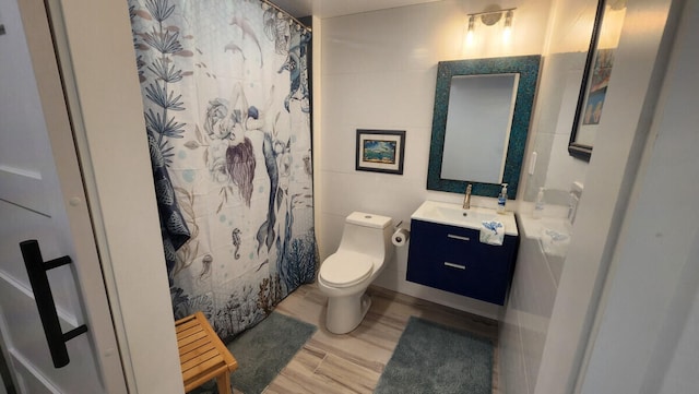 bathroom featuring tile walls, hardwood / wood-style flooring, vanity, walk in shower, and toilet