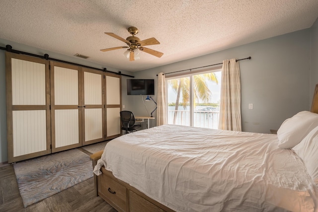 bedroom featuring dark parquet flooring, access to exterior, ceiling fan, a barn door, and a textured ceiling