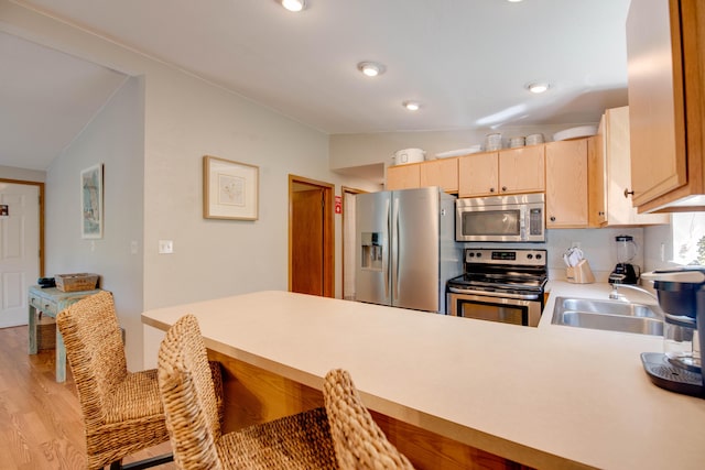 kitchen featuring lofted ceiling, stainless steel appliances, light brown cabinetry, and sink