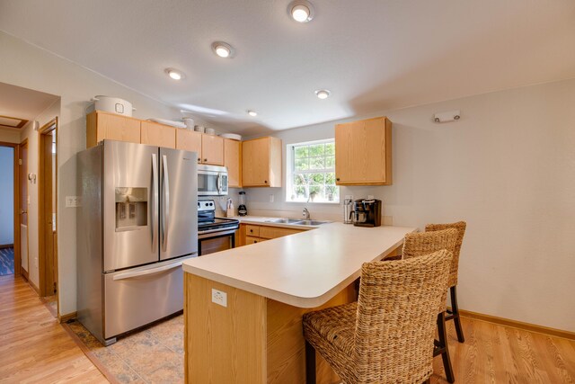 kitchen with appliances with stainless steel finishes, light brown cabinetry, sink, a breakfast bar area, and kitchen peninsula