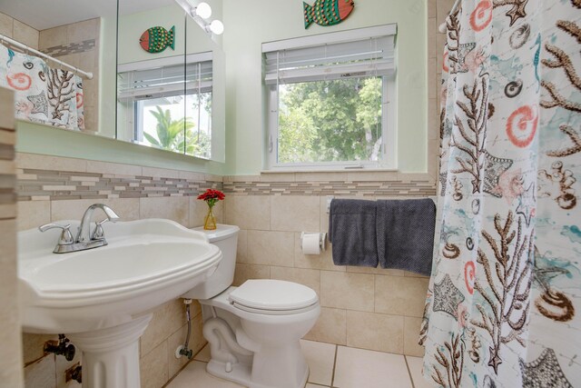 bathroom with a healthy amount of sunlight, toilet, tile patterned flooring, and tile walls