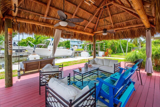 wooden terrace featuring a gazebo, ceiling fan, an outdoor hangout area, and a water view