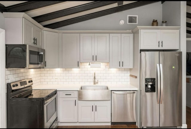 kitchen featuring appliances with stainless steel finishes, vaulted ceiling with beams, white cabinets, backsplash, and sink