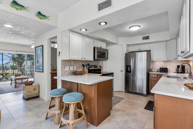 kitchen featuring a breakfast bar, sink, tasteful backsplash, stainless steel appliances, and white cabinets