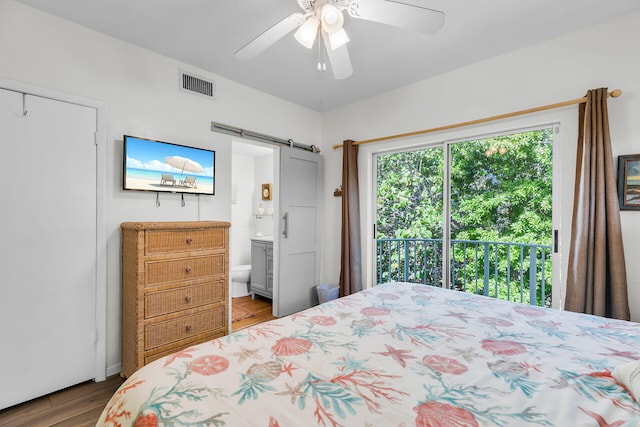 bedroom with wood finished floors, visible vents, ensuite bath, ceiling fan, and a barn door