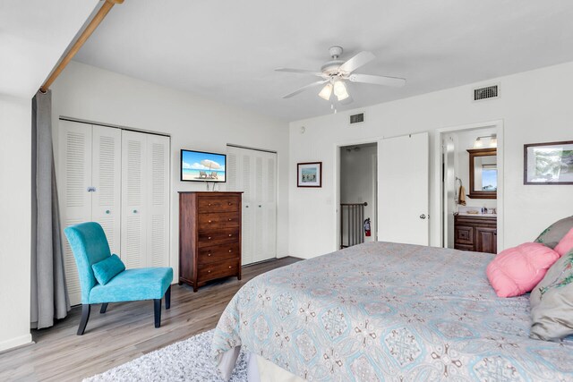 bedroom featuring two closets, ensuite bathroom, ceiling fan, and light wood-type flooring