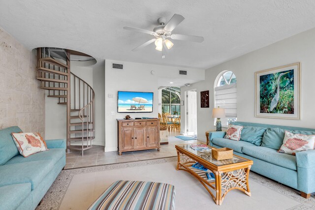 living room with light tile patterned floors, a ceiling fan, visible vents, stairs, and a textured ceiling