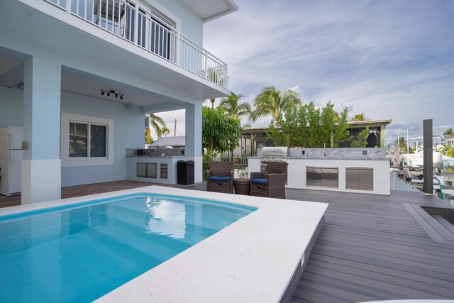 view of swimming pool featuring a wooden deck, area for grilling, and exterior kitchen