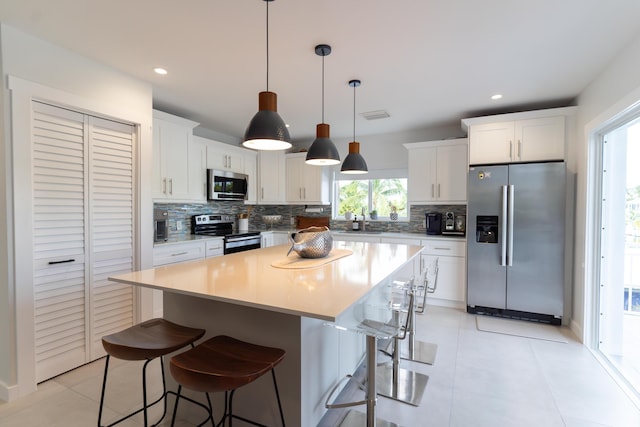 kitchen featuring white cabinetry, appliances with stainless steel finishes, a center island, and decorative light fixtures