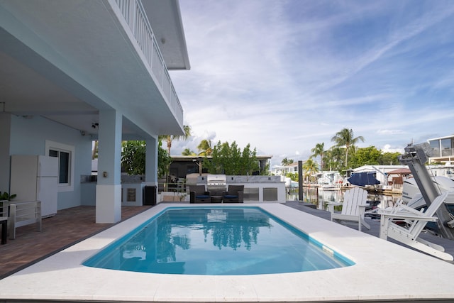 view of pool featuring a water view, area for grilling, exterior kitchen, and a patio area