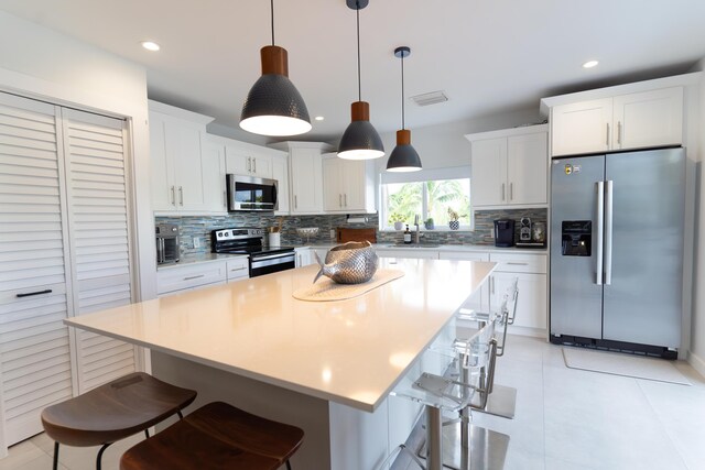 kitchen with a kitchen island, appliances with stainless steel finishes, white cabinets, and decorative light fixtures