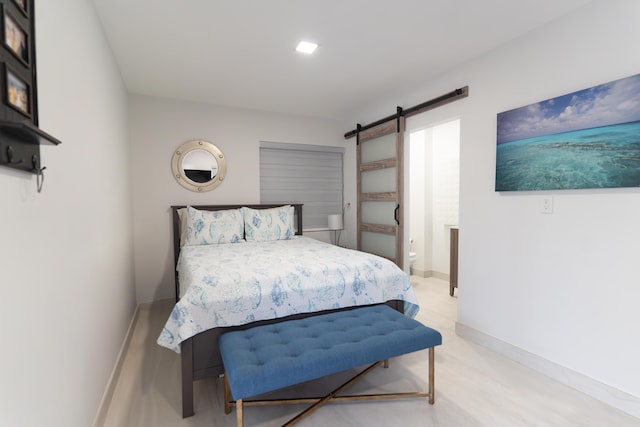 bedroom with ensuite bath, a barn door, and light wood-type flooring