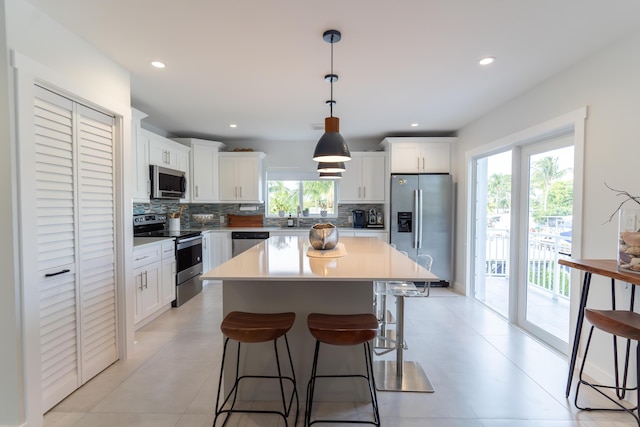 kitchen with tasteful backsplash, hanging light fixtures, a kitchen island, stainless steel appliances, and white cabinets