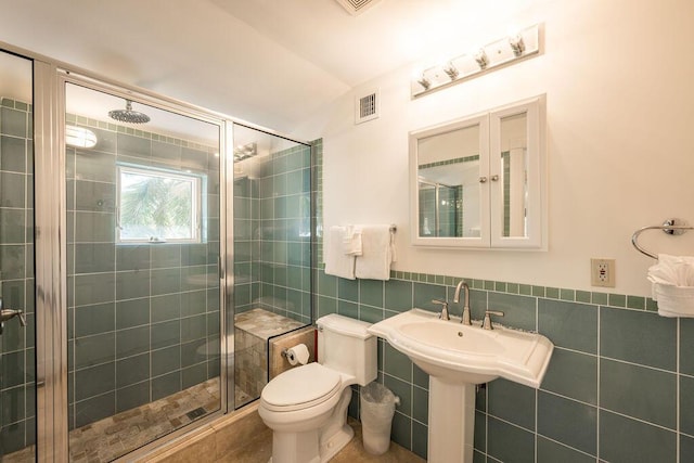 bathroom featuring toilet, a shower with door, and tile walls