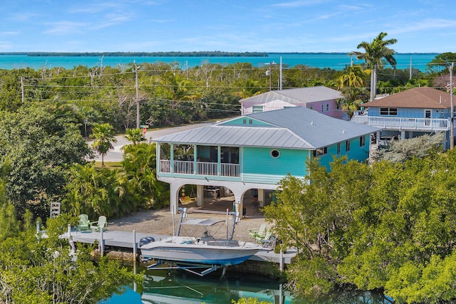 back of property with boat lift, a water view, and metal roof