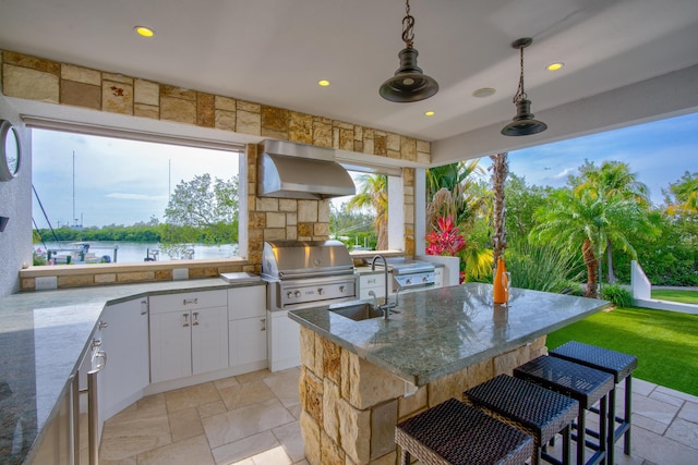 view of patio / terrace with ceiling fan, a water view, a grill, an outdoor kitchen, and exterior bar