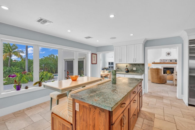 kitchen featuring a center island, stainless steel built in fridge, light stone countertops, decorative backsplash, and white cabinets