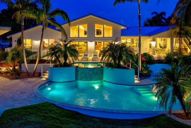 pool at night with an in ground hot tub and a patio