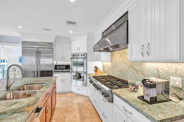 kitchen with appliances with stainless steel finishes, sink, white cabinets, light stone countertops, and wall chimney exhaust hood