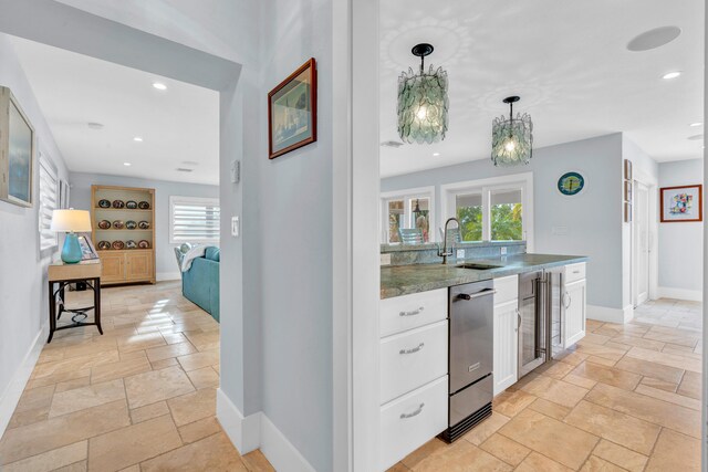 kitchen featuring white cabinetry, sink, stainless steel dishwasher, and decorative light fixtures