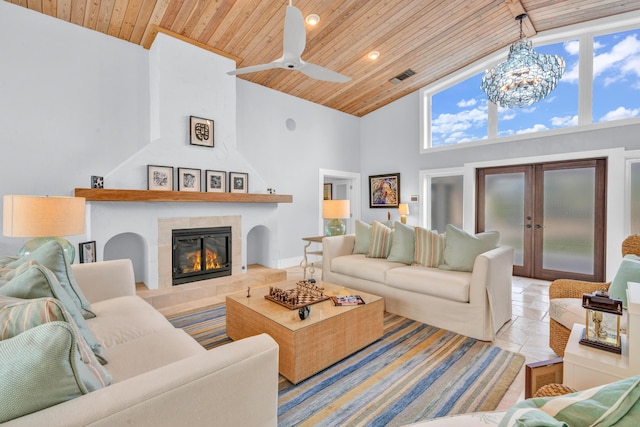 tiled living room with ceiling fan with notable chandelier, high vaulted ceiling, a fireplace, wood ceiling, and french doors