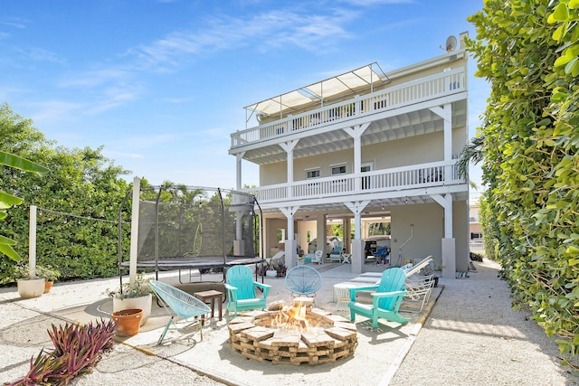 rear view of house featuring a trampoline, a patio, a balcony, and an outdoor fire pit