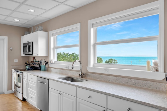 kitchen featuring sink, a water view, white cabinetry, light stone counters, and appliances with stainless steel finishes