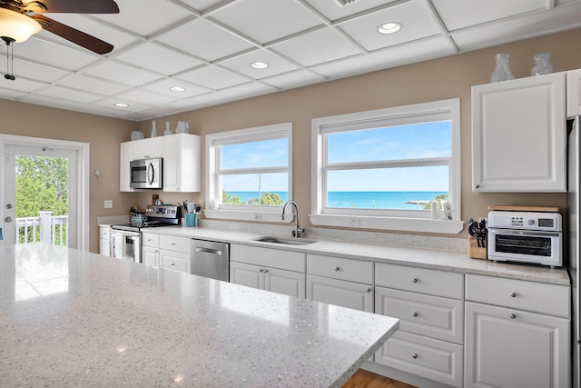 kitchen featuring sink, appliances with stainless steel finishes, a water view, a wealth of natural light, and white cabinets