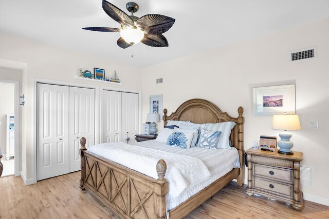 bedroom with ceiling fan, light hardwood / wood-style floors, and two closets