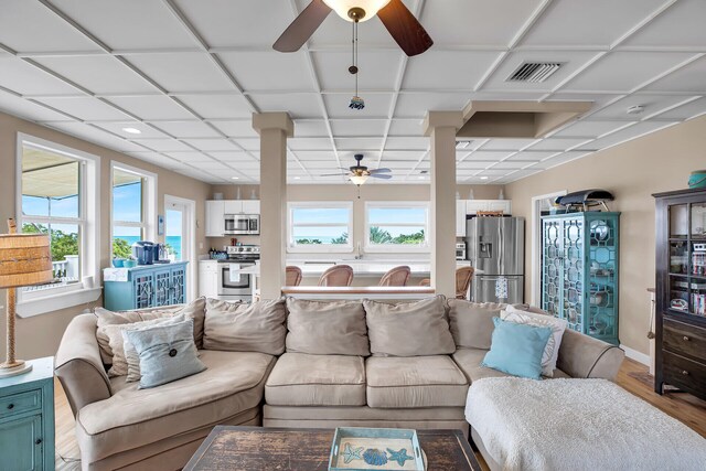 living room with a drop ceiling, wood-type flooring, a wealth of natural light, and ceiling fan