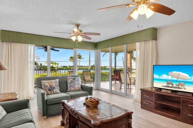 living room featuring a textured ceiling, ceiling fan, a wealth of natural light, and light wood-style floors