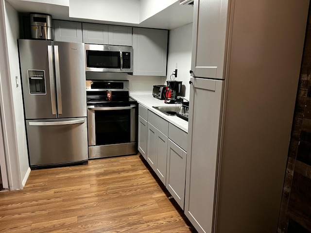 kitchen featuring stainless steel appliances, gray cabinetry, a sink, and light wood-style floors