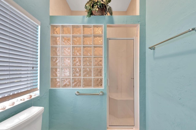 bathroom with toilet, a stall shower, and a textured wall