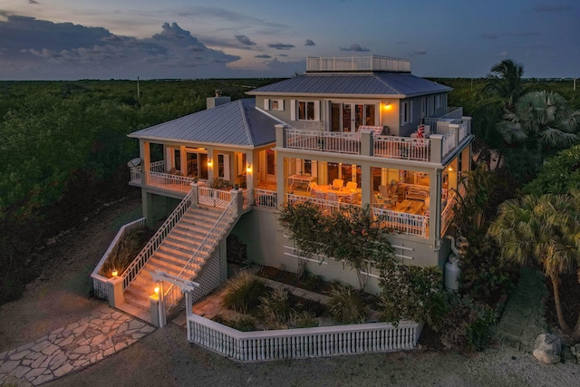 back of house with a garage, a balcony, stairway, metal roof, and covered porch