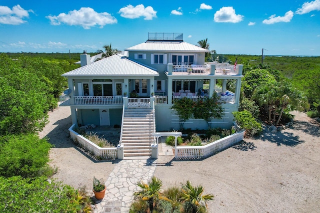 rear view of property featuring a balcony, a chimney, stairway, metal roof, and a standing seam roof