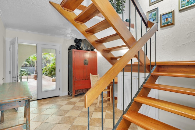 staircase featuring ceiling fan, ornamental molding, and a textured ceiling