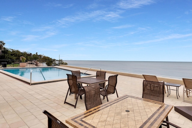 view of swimming pool featuring a water view, a beach view, and a patio area