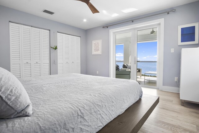 bedroom with a water view, light wood-type flooring, multiple closets, access to outside, and ceiling fan