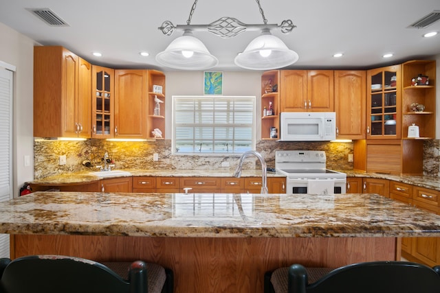 kitchen featuring sink, white appliances, a breakfast bar area, light stone countertops, and decorative light fixtures